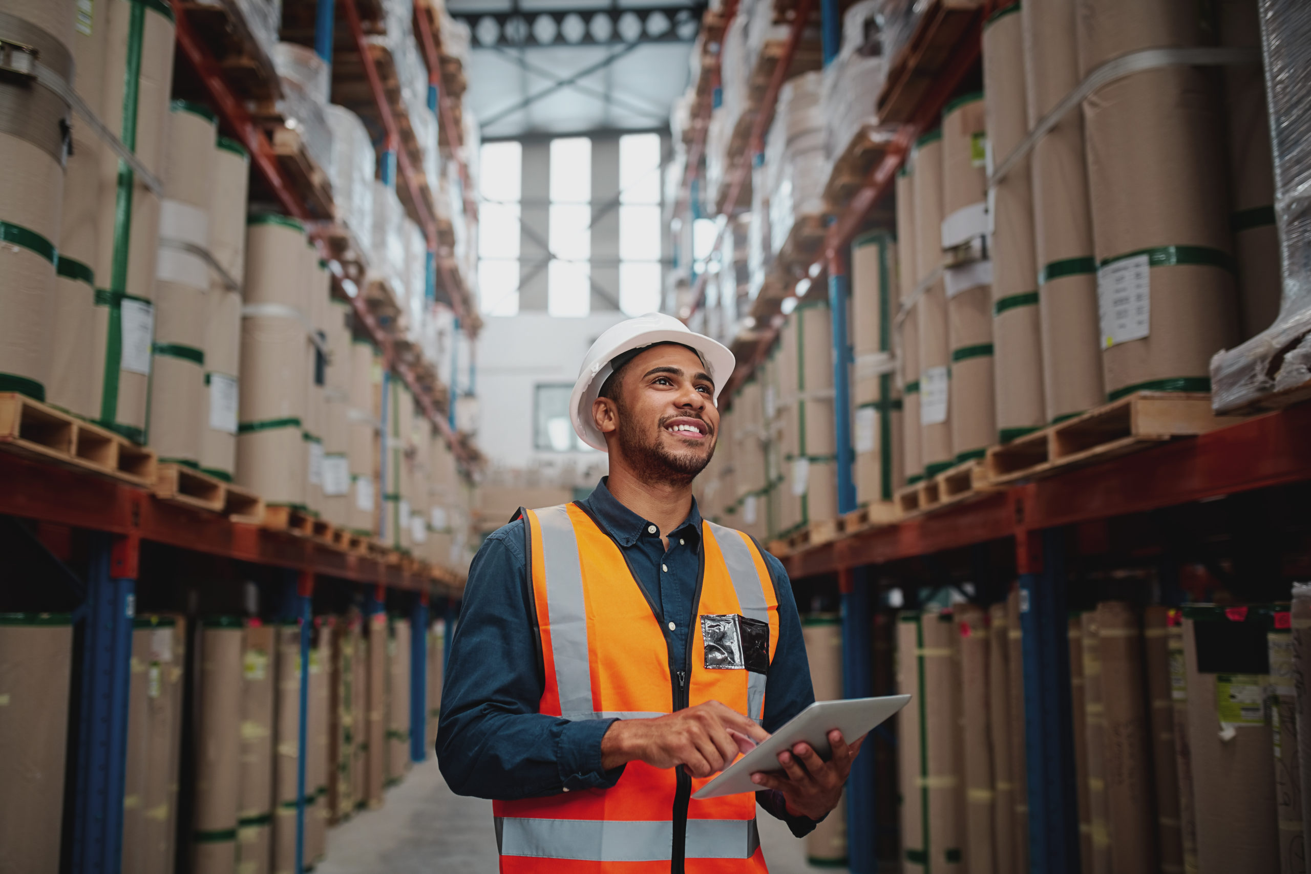 Portrait d'un jeune homme portant un gilet de sécurité et tenant une tablette numérique dans un entrepôt d'usine.